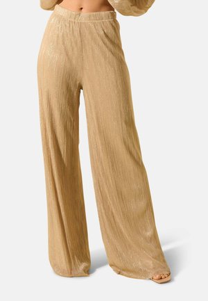 Pantalons larges dorés avec une surface brillante et texturée, dotés d'une taille haute et d'un motif côtelé vertical. L'ourlet tombe près des chevilles.