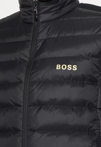 Svart vadderad jacka med framdragkedja och "BOSS"-logotyp i ljusbeige på vänster bröst.