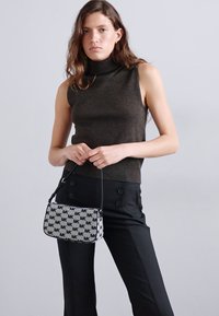 Black and white printed handbag with "MK" logo, flat design, adjustable strap, paired with a dark sleeveless top and black trousers.