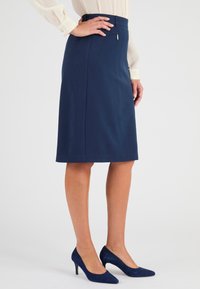 Jupe crayon bleu marine avec une coupe ajustée, texture lisse et une poche zippée sur le côté. Complétée par des talons assortis.