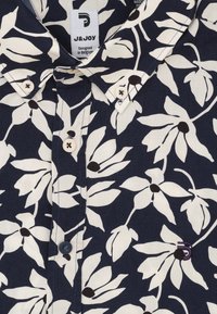 Marineblauw bloemetjesoverhemd met ivoorkleurige bladeren en zwarte centra. Met knopen naar beneden stijl met witte knopen en een label met de naam J&JOY.