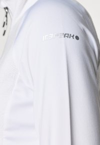 Jaqueta atlética branca com um padrão texturizado de um lado, apresentando um logotipo refletor "ICEPEAK" no ombro. Tecido suave e leve.