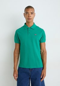 Zelené polo tričko z bavlny s klasick�ým golierom, trojicou gombíkov a malým červeným logom Levi's na hrudi.