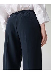 Marineblauwe broek met een relaxte pasvorm, voorzien van een gegatherde elastische tailleband en een enkele achterzak. Glad, lichtgewicht materiaal.