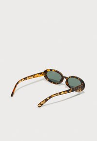 Tortoiseshell zonnebril met ovale lenzen en groene tint. Slanke pootjes hebben een lichte glanzende textuur met donkere patronen.