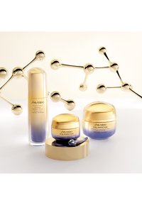 Shiseido Vital Perfection hudvårdssats: inkluderar en hög serumflaska och två krämburkar, alla med guld- och lila gradientdesign.