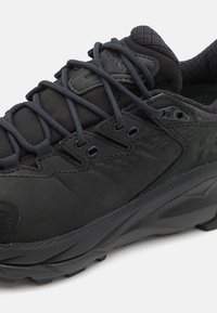 Černá sportovní obuv s texturovaným svrškem, síťovanými panely a silnou, odolnou podešví. Obsahuje černé tkaničky a otvory pro tkaničky pro bezpečné uchycení.