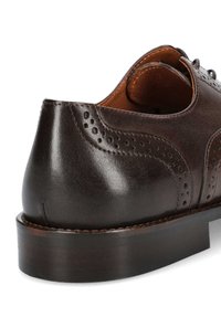 Ciemnobrązowe skórzane buty wizytowe o gładkiej fakturze, z fasonem wingtip, perforowanymi detalami i piętką wykonaną z warstw, które pokazują rzemiosło i trwałość.