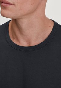 Donkergrijze katoenen t-shirt met een ribgebreide ronde halslijn, een gladde textuur en subtiele stiksels op de kraag en schouder.