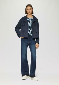 Marineblauwe cropped jacket met dubbelzijdige knopen, lichtblauw graphic top, donkerdenim wide-leg jeans en witte platform sneakers.