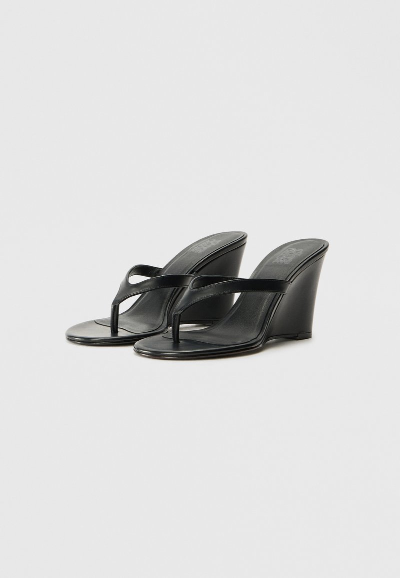 Sandalias de cuña negras con un acabado de cuero suave, punta descubierta y correa estilo thong. El tacón es alto y angular, añadiendo un diseño moderno.