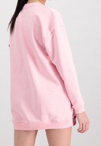 Różowa bluza o luźnym kroju, z długimi rękawami i ściągaczami na mankietach, posiadająca metkę na dolnym brzegu oraz gładką, bawełnianą fakturę.