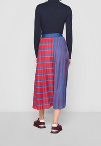 Jupe longue plissée avec une combinaison de rayures verticales rouges et bleues, dotée d'une taille bleue unie. Portez-la avec des baskets sombres.