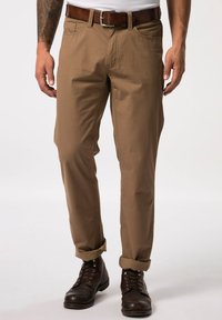 Beige Baumwollhosen mit geradem Bein, aufgeschlagenen Säumen und Fronttaschen, kombiniert mit dunkelbraunen Lederstiefeln und einem braunen Gürtel.