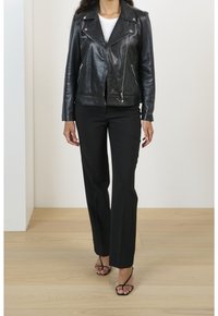 Svart läderbikerjacka med jackslag, dragkedja framtill och två sidofickor, kombinerad med svarta skräddarsydda byxor och sandaler med tunna remmar.