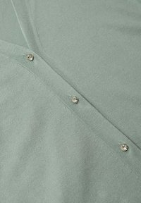 Jasnozielony sweter z dzianiny, z dekoltem w szpic i ozdobnymi okrągłymi guzikami z metalicznymi akcentami wzdłuż przedniej listwy.