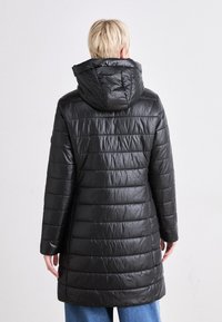 Svart, lang puffjakke med horisontalt quiltet design, overdimensjonert hette og glatt, blank overflate. Har lange ermer og en avslappet passform.