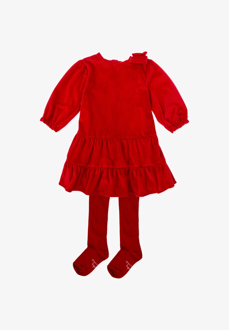 Vestido de terciopelo rojo con mangas largas abullonadas, falda con volantes y un lazo en el hombro. Combinado con unas medias rojas a juego.