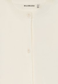 Bela jopica z diskretnim leskom, s krojem okroglega vratu, zapiranjem na gumbe in mehkim, teksturiranim materialom.