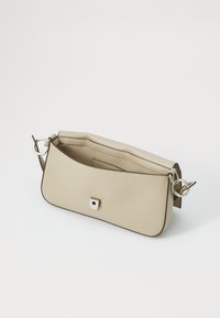 Borsa a spalla in pelle beige con una texture liscia, design curvato, chiusura a patta, accessori in metallo argentato e un semplice accento quadrato sulla parte anteriore.