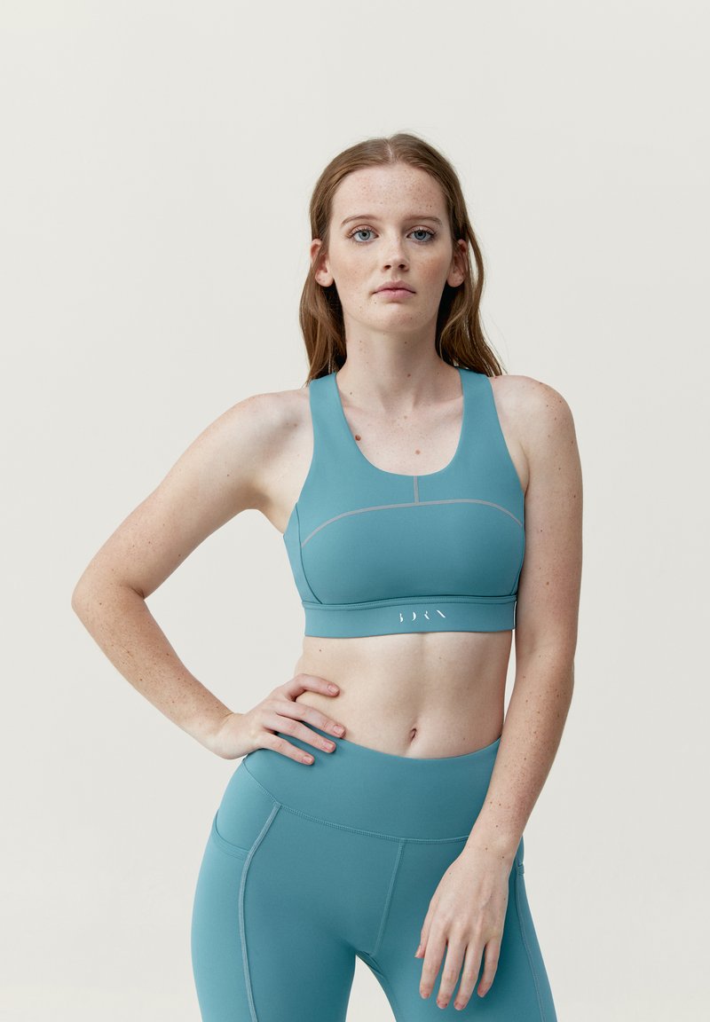 Ljusblå sportbh med breda band, slät yta och en figurnära design. Har diskret sömnad och en logo på framre bandet.