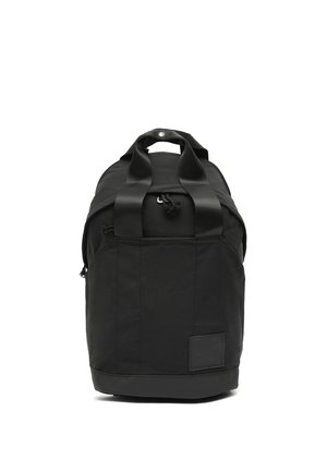 Bolsa de lona negra con dos asas, cierre de cremallera y un pequeño parche en la parte frontal inferior, sobre un fondo blanco.