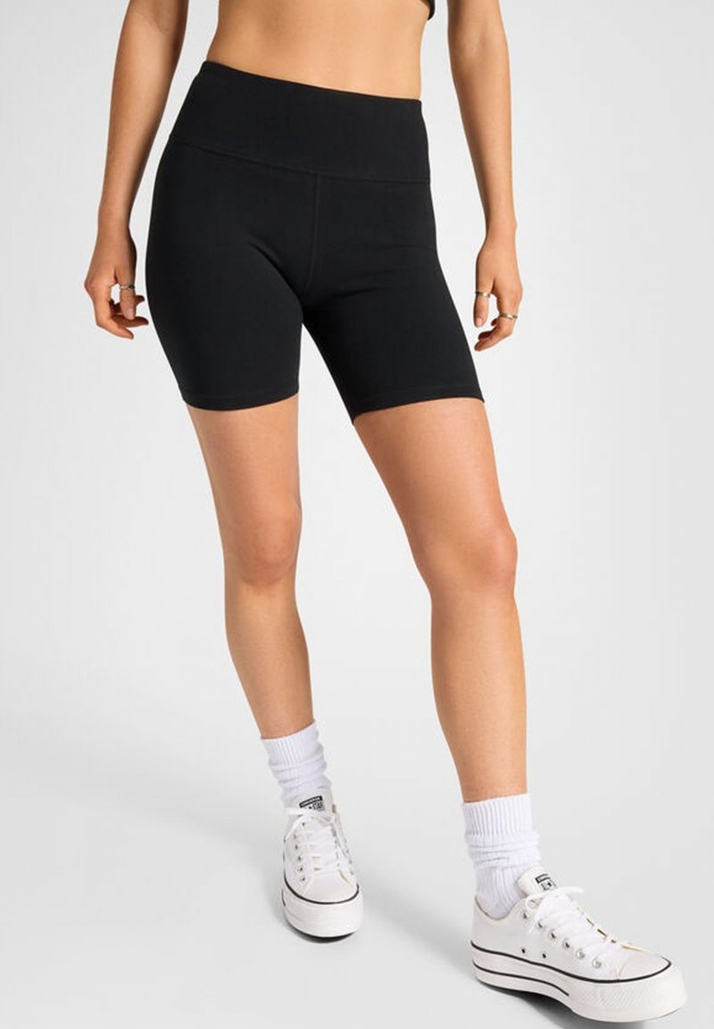 Pantalones cortos de ciclismo negros de talle alto, fabricados en un tejido elástico, con una textura suave y un diseño ajustado, combinados con zapatillas blancas y calcetines.