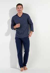 Navy loungewear set featuring a long-sleeve shirt with a polka dot pattern and solid navy pants. Cotton blend material, relaxed fit design.