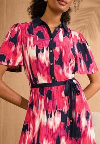 Abito a camicia in un motivo astratto rosa, blu navy e bianco. Caratterizzato da maniche a sbuffo corte, vita legata e gonna plissettata. Bottoni color oro.
