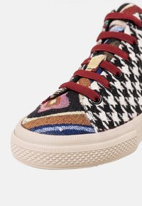 Baskets avec lacets bordeaux, motif pied-de-poule noir et blanc, tissu géométrique multicolore sur le bout et les côtés, semelle en caoutchouc beige.