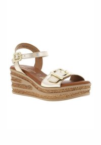 Sandale compensée en métal doré avec une bride de cheville, présentant une grande boucle et des détails en jute tissé sur la plateforme. Semelle intérieure rembourrée marron.