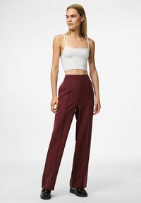 Pantalons bordeaux à rayures avec une coupe droite, une taille haute et une texture lisse. Associés à un crop top blanc ajusté et des chaussures noires.