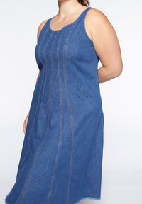 Denimklänning med utan ärmar-design, rundad halsringning och vertikala sömdetaljer. Kanten är något fransad. Färg: blå.