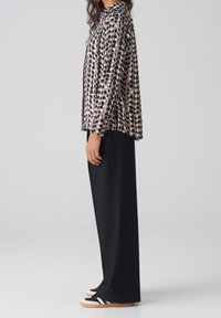 Polka dot blouse in beige and black, long sleeves, loose fit, paired with black wide-leg pants and black sneakers with white stripes.