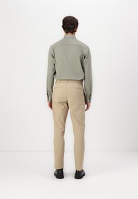 Khaki chinos med elastisk midjebånd, slim fit. Kombinert med en olivengrønn skjorte med krage, begge laget av glatt stoff. Svarte sko brukt.