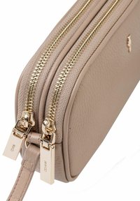 Beżowa skórzana torba z dwiema złotymi suwakami, posiadająca teksturowaną powierzchnię oraz smukły, prostokątny kształt. Widoczne akcenty z markowym metalem.