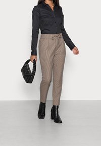 Black, long-sleeved button-up shirt paired with patterned beige trousers, ankle-high black heeled boots, and a black braided handbag.