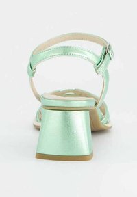 Jemně zelené metalické sandály na podpatku s otevřenou zadní částí, nastavitelným páskem kolem kotníku a texturovaným blokovým podpatkem. Hladká stélka a lehká gumová podešev.