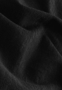 Gros plan d’un tissu noir doux avec une texture tricot visible et des plis créant des ombres douces et de la profondeur.