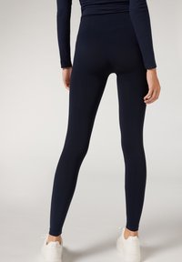 Marine leggings lavet af strækstof, med en høj talje og en glat tekstur. Bruges med hvide sneakers, set fra ryggen.