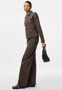 Brun denimjacka och byxor setet har en klassisk design med sidofickor och silverknappar. Kombineras med en strukturerad svart handväska.