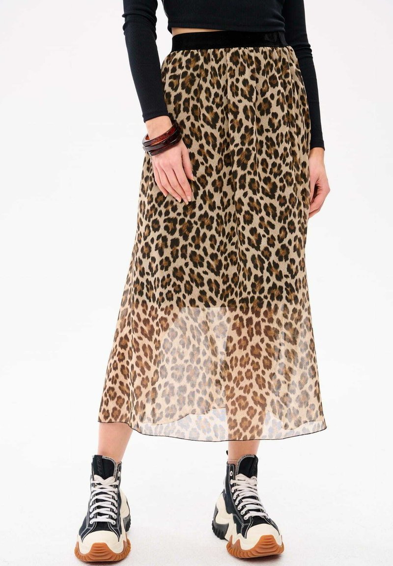Leopardprint midi-rok van doorzichtig materiaal, met een zwarte elastische tailleband. Gecombineerd met zwart-witte high-top sneakers.