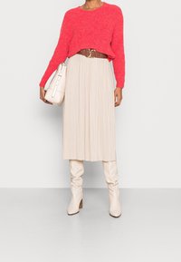 Ljusrosa stickad tröja, beige veckad midiklänning, krämfärgade slappa knästövlar och en vit strukturerad handväska i rundad form.