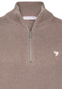 Brauner Reißverschluss-Pullover aus weichem Material, mit hohem Kragen, silbernem Reißverschluss und kleinem weißen Vogel-Logo auf der linken Brust. Glatte Textur.