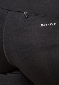 Gros plan sur un legging de sport noir avec une petite poche zippée et le logo blanc "DRI-FIT" sur la hanche.