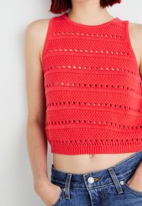 Rode gebreide crop top met een gestructureerd patroon met horizontale strepen en opengewerkte details. Gecombineerd met hoge denim shorts.