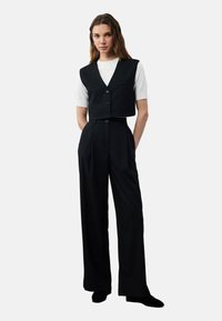 Zwarte cropped top met een V-hals en knopen, gecombineerd met hoge zwarte wijde broek. Witte korte mouw shirt eronder.