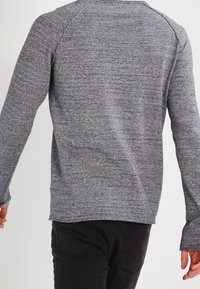 Grå långärmad skjorta i ett strukturerat, stickat tyg. Har raglanärmar och rundad halsringning. Bärs med svarta byxor.