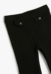 Pantalones negros de canalé con dos bolsillos de solapa abotonados en la parte delantera de la cinturilla, mostrados planos sobre un fondo blanco.