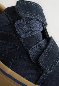 Baskets en tissu bleu marine avec des bandes velcro, textures contrastantes et semelle en caoutchouc. Présente des accents cousus et un bout arrondi.